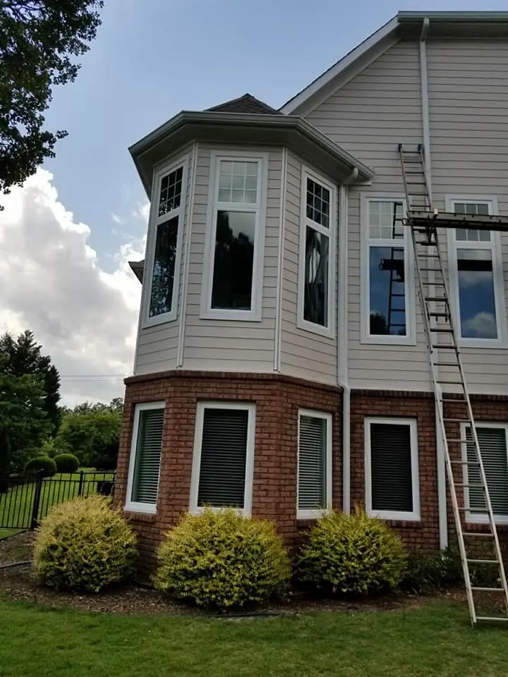 Two-story home with brick lower level and bay windows, with a ladder set against the gutters